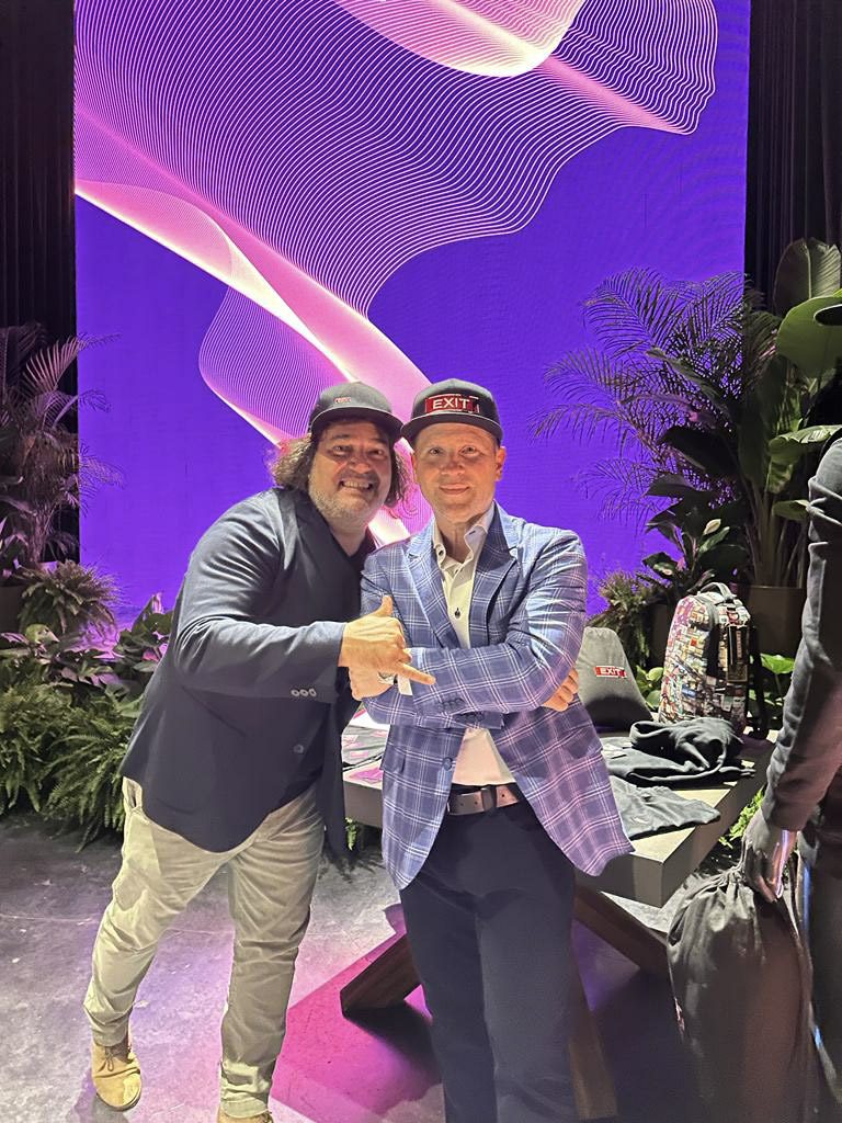 Two men smiling and shaking hands on stage with purple lighting.