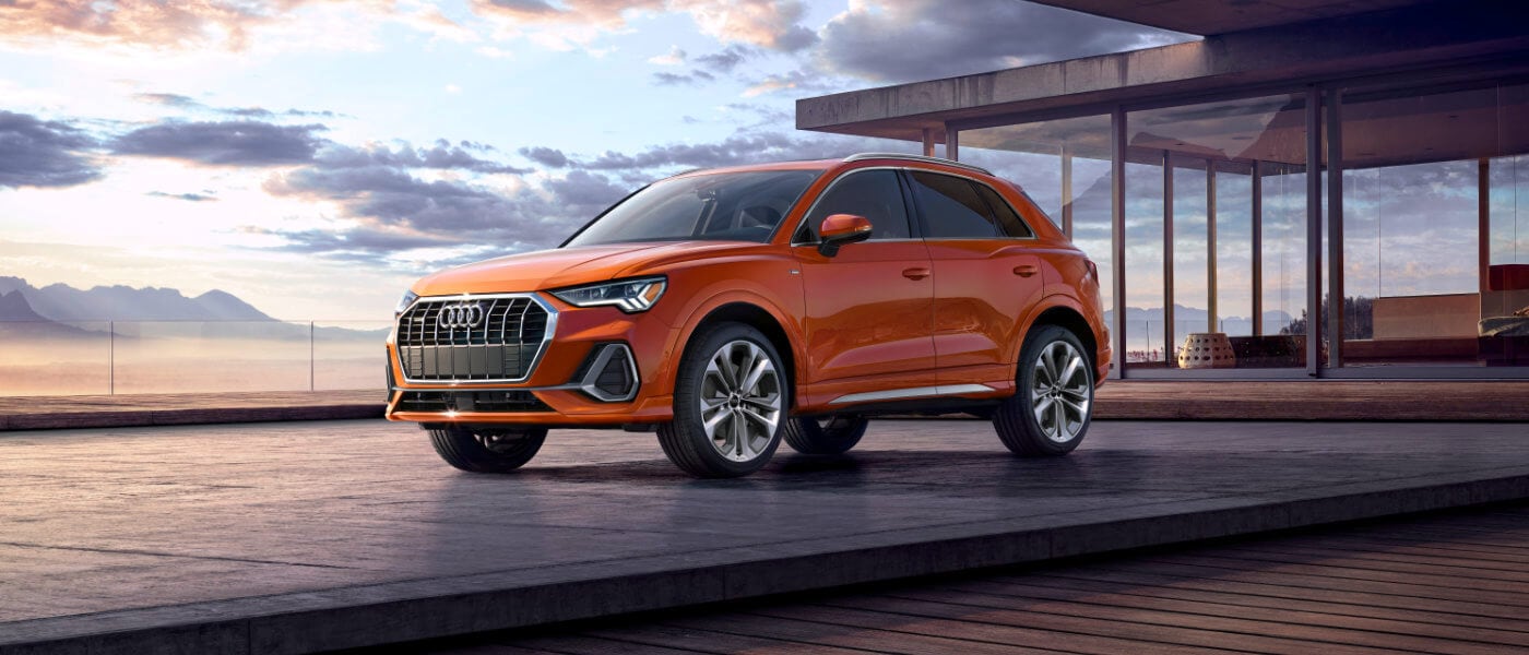 Orange Audi SUV parked on modern rooftop at sunset.