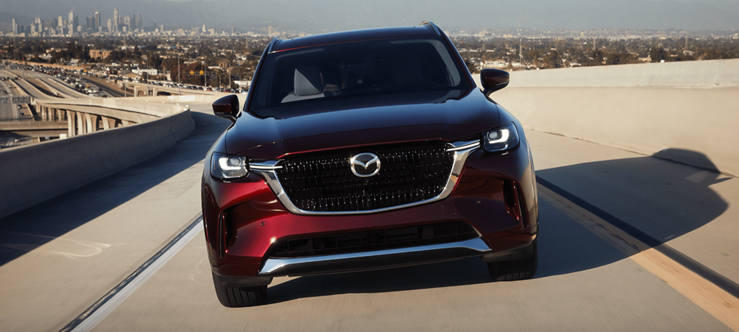 Red Mazda SUV driving on a road with cityscape in the background.