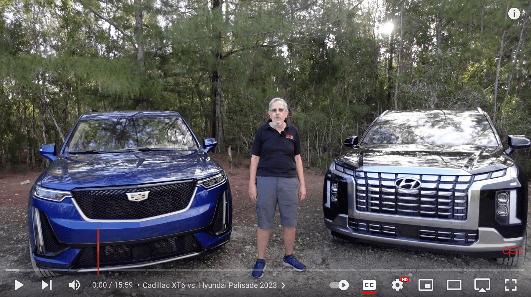 Man standing between two black SUVs in a wooded area.