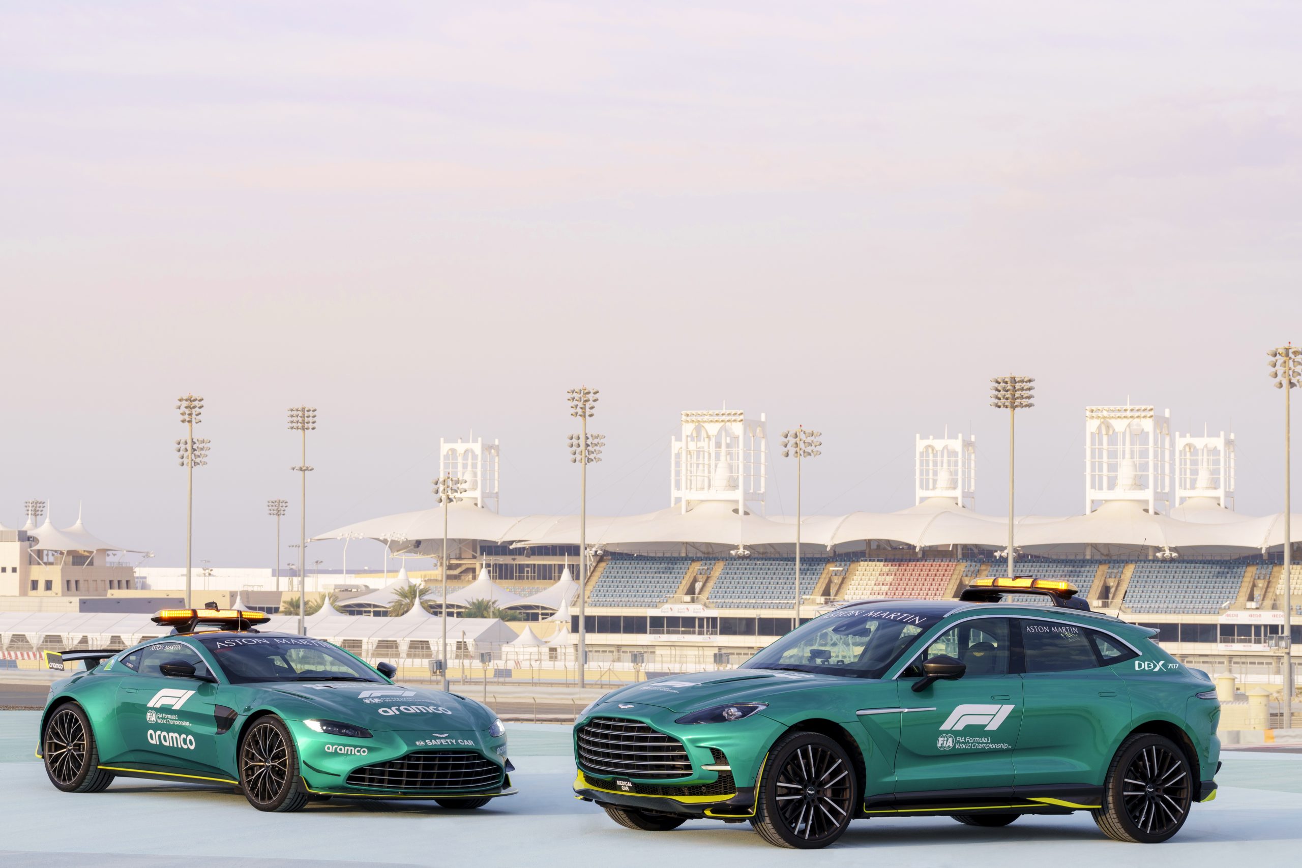 Two green Jaguar cars parked near a stadium under a clear sky.