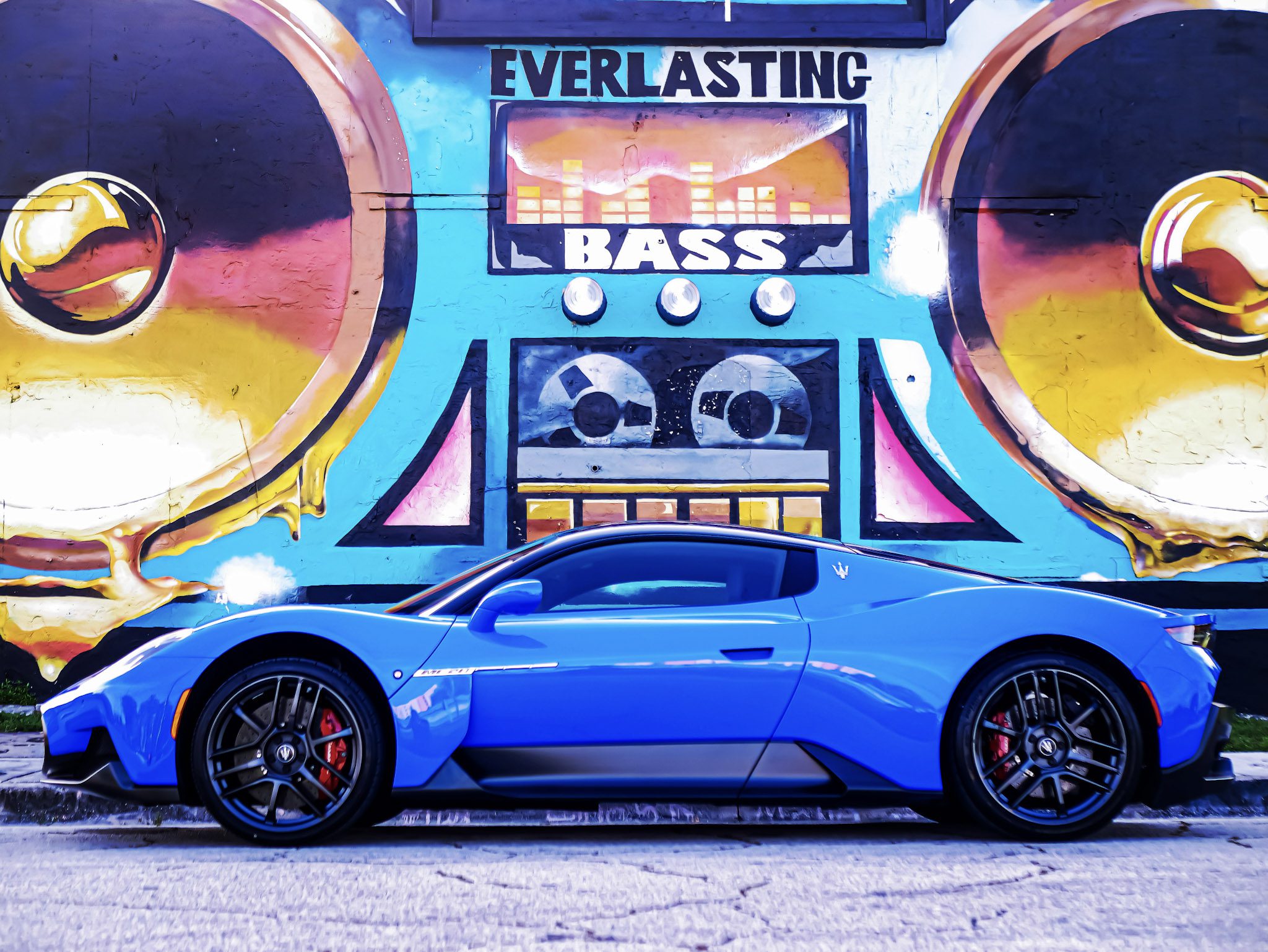 Blue sports car parked in front of a colorful DJ speaker mural.