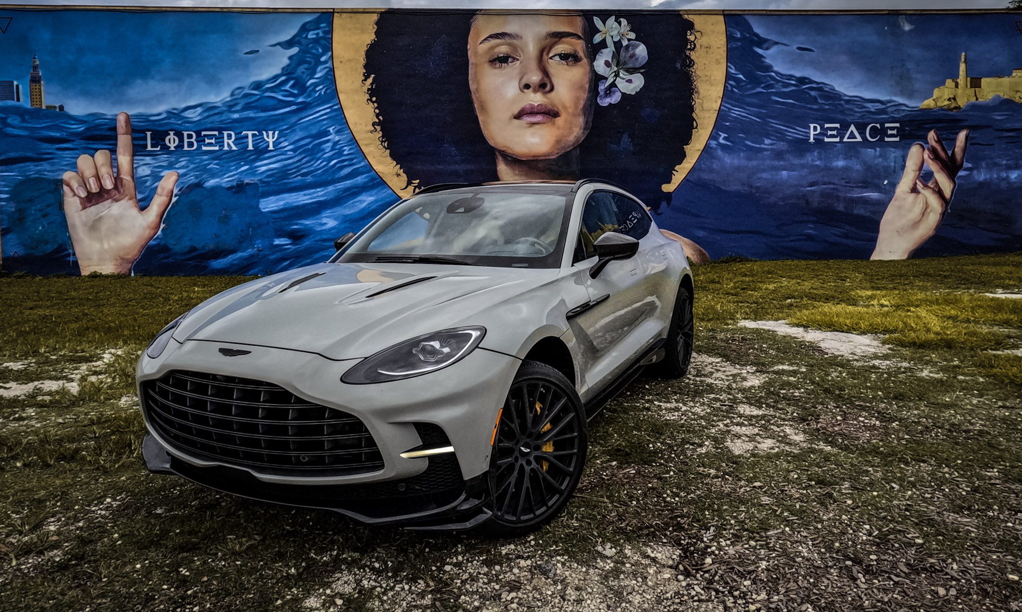 Sleek silver sports car parked in front of a vibrant mural of a woman with a blue background.