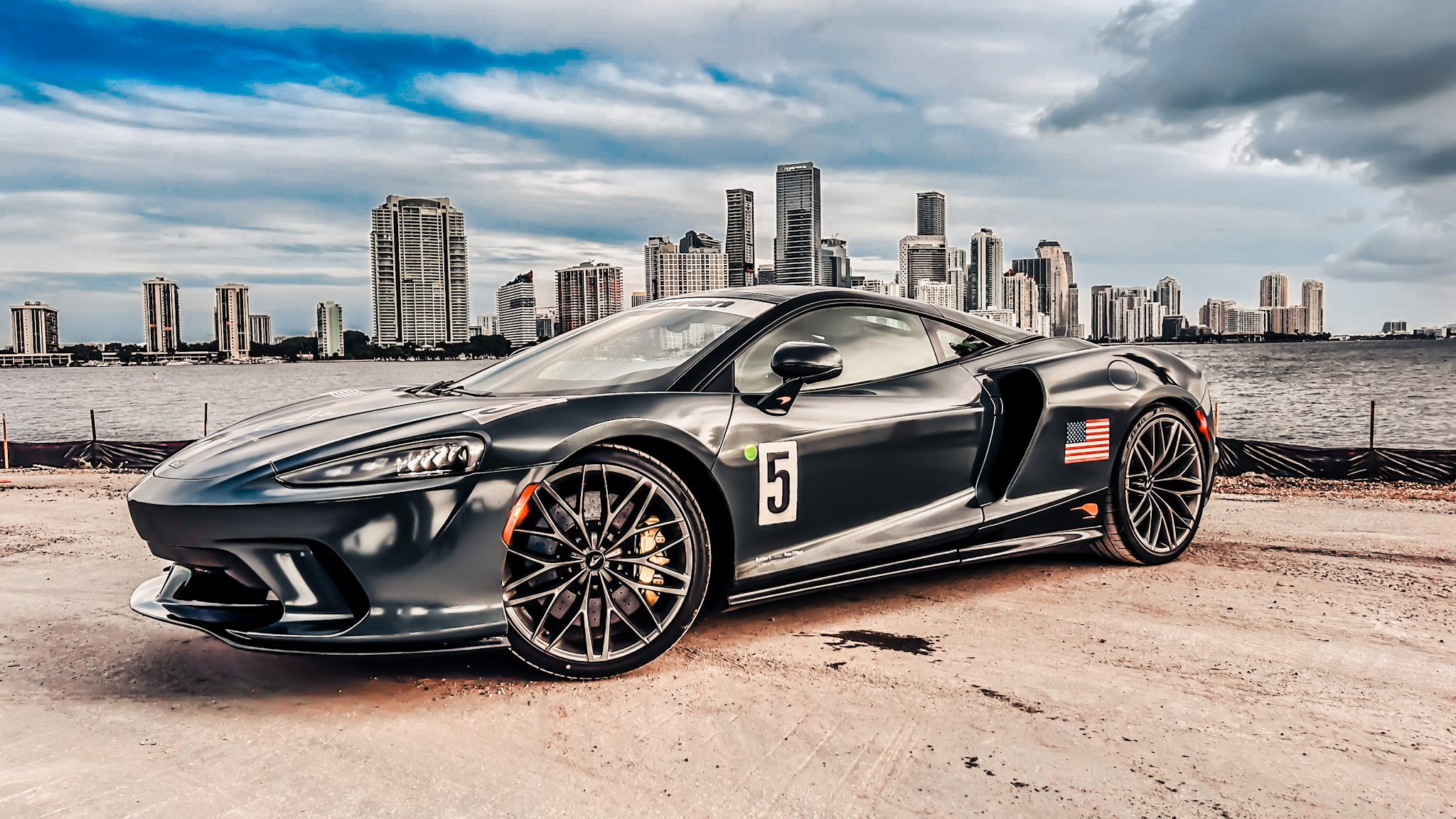 Black sports car parked with city skyline in background.