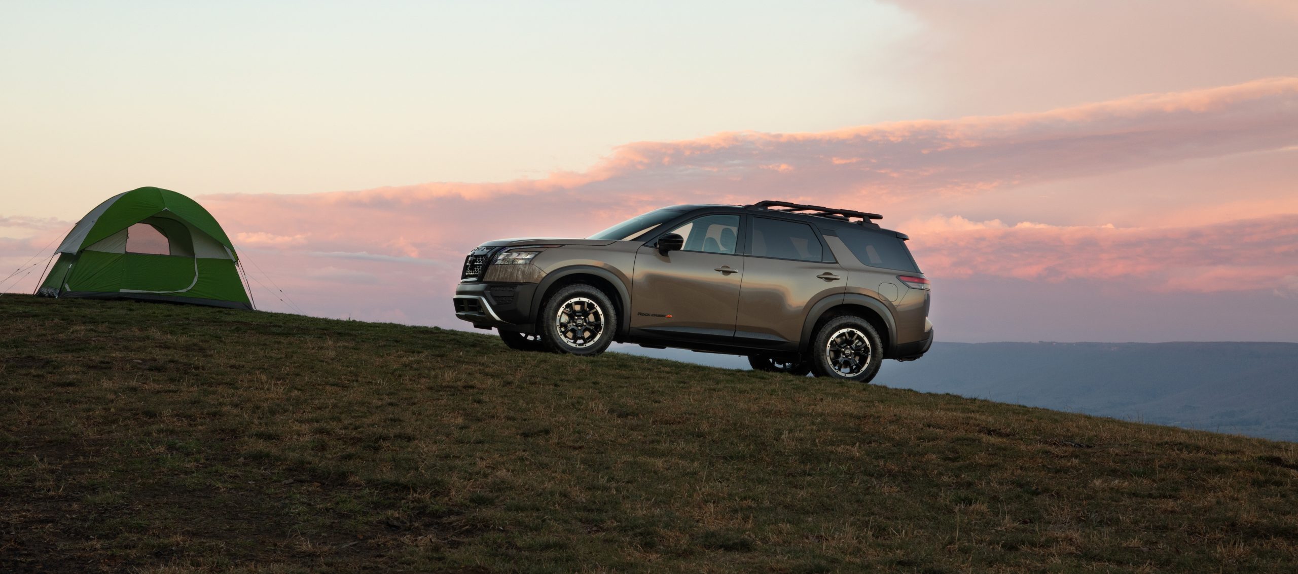 SUV parked on a grassy hill with a sunset sky.