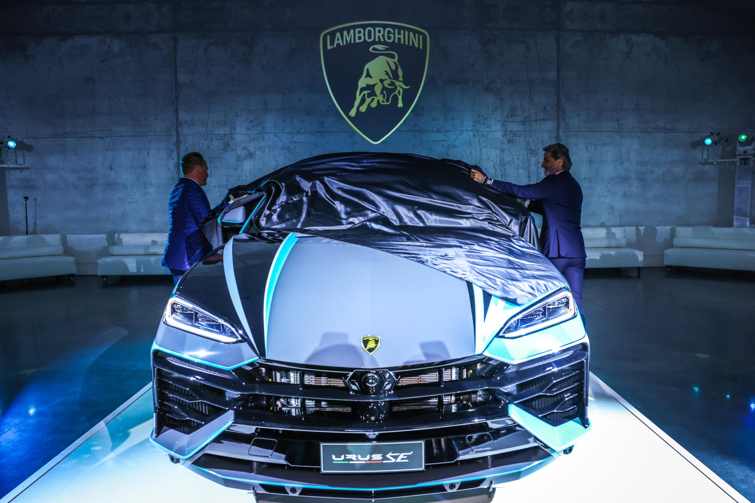 Two men unveiling a Lamborghini car in a dramatic setting.