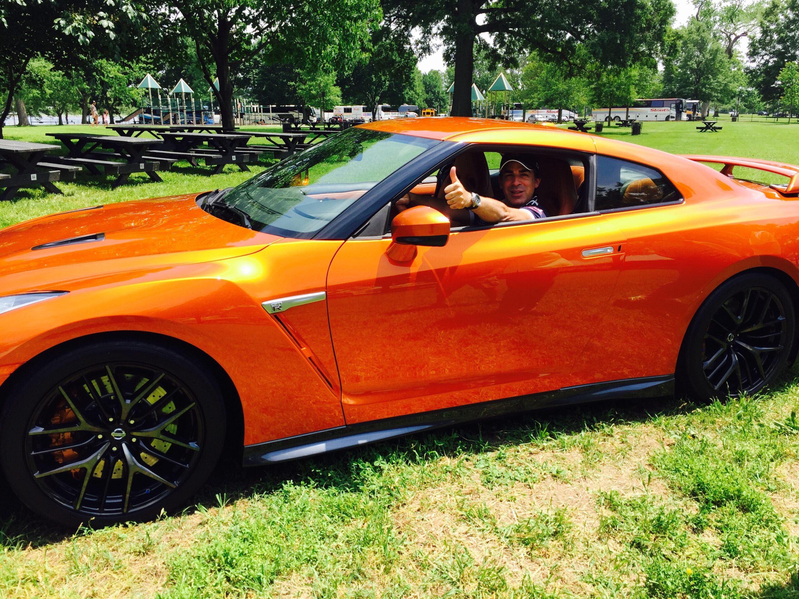 Person sitting inside an orange sports car parked on grass.