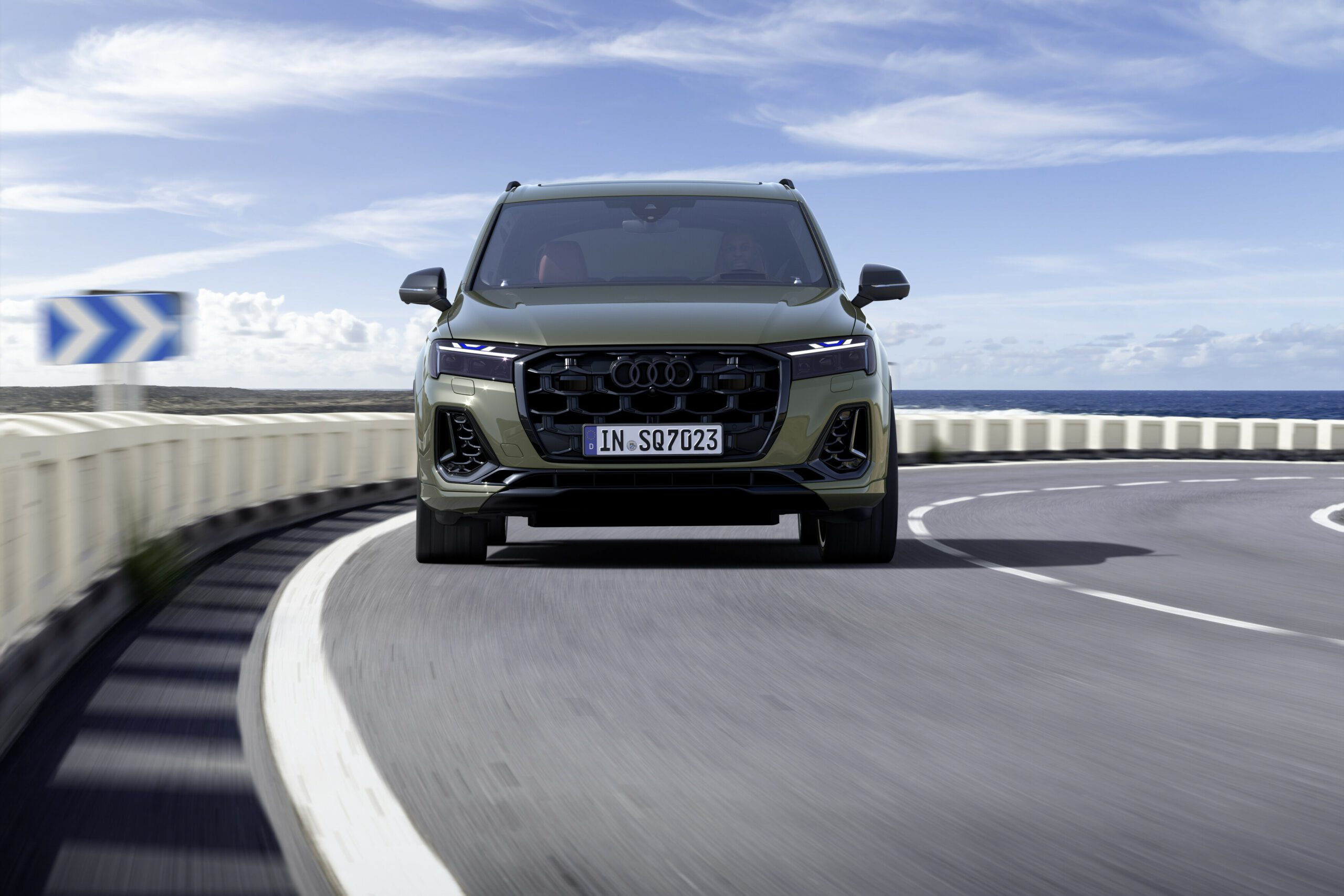 Front view of a modern black SUV on a curved road under a blue sky.
