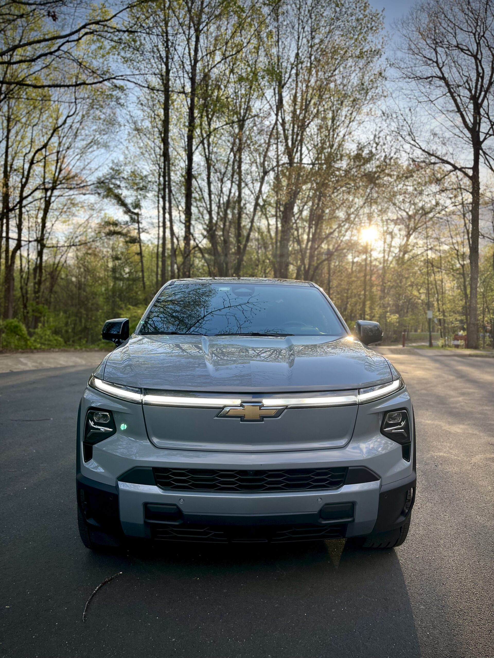 Front view of a modern silver Chevrolet SUV on a forest-lined road.