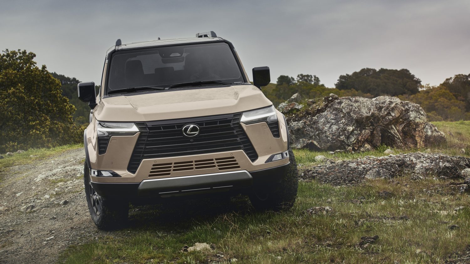 A rugged beige SUV parked on grassy terrain with rocky hills in the background.