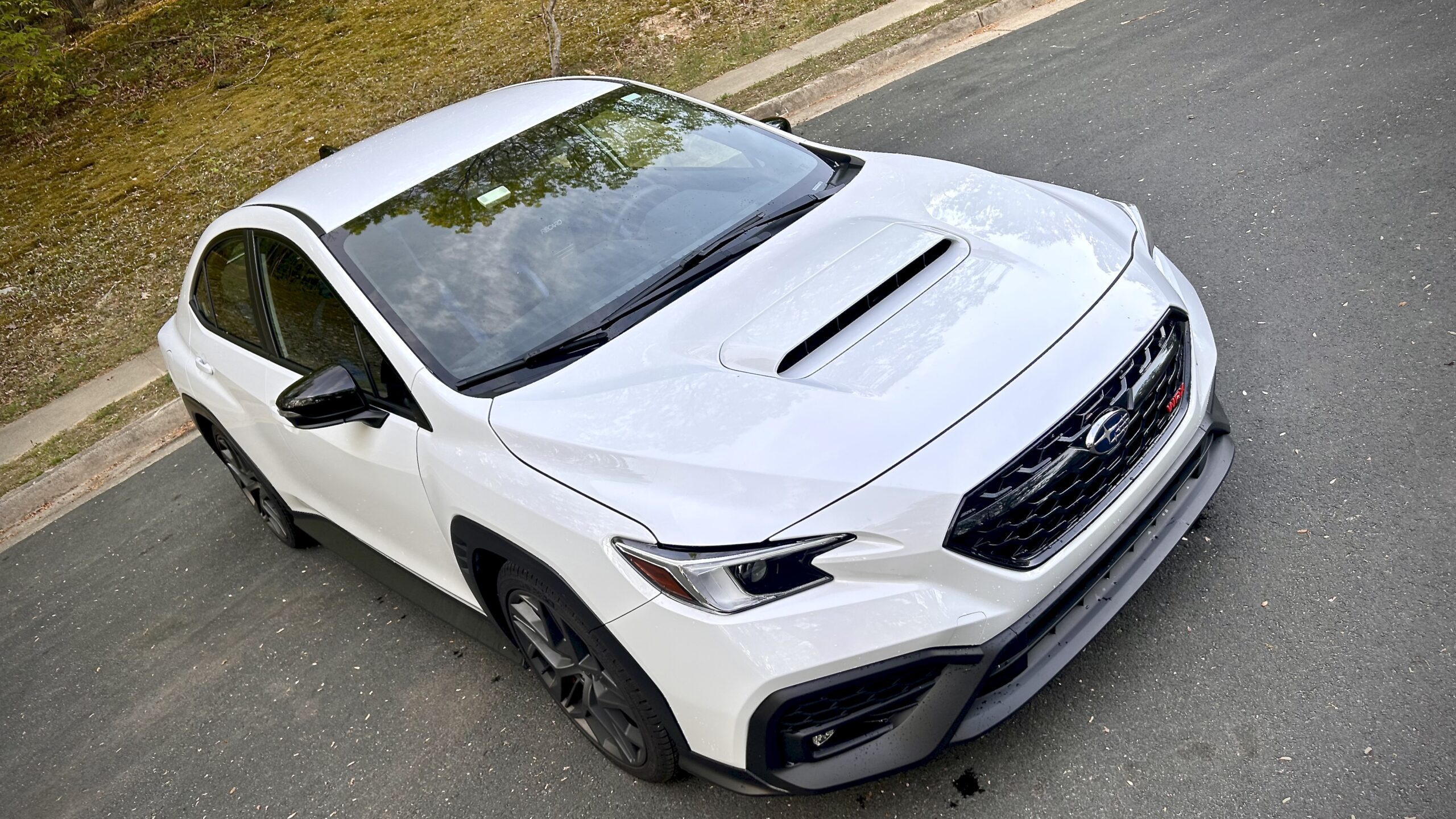 White sporty sedan parked on the street under sunlight.