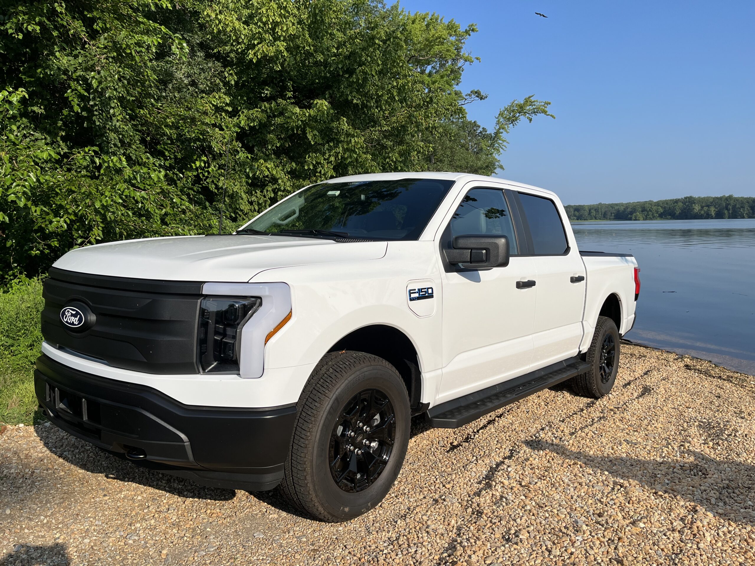 White pickup truck parked on a gravel path near greenery and water.