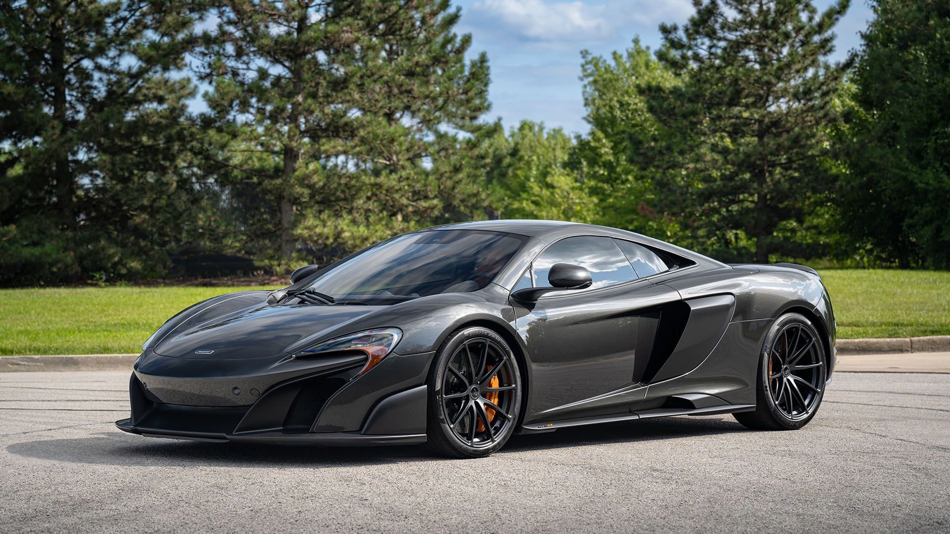 Sleek black sports car parked with trees in the background.