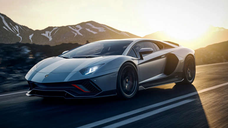 A sleek gray sports car driving on a mountain road at sunset.