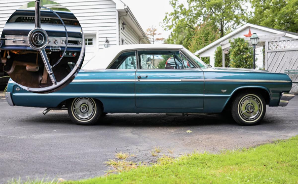 A vintage blue car parked on a driveway beside a white house.