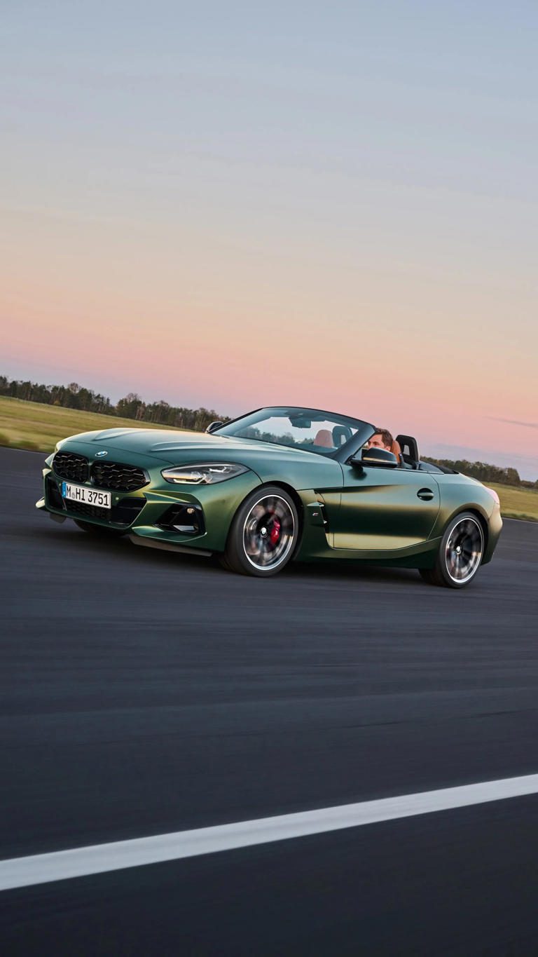 A sleek green convertible sports car driving on an open road at sunset.