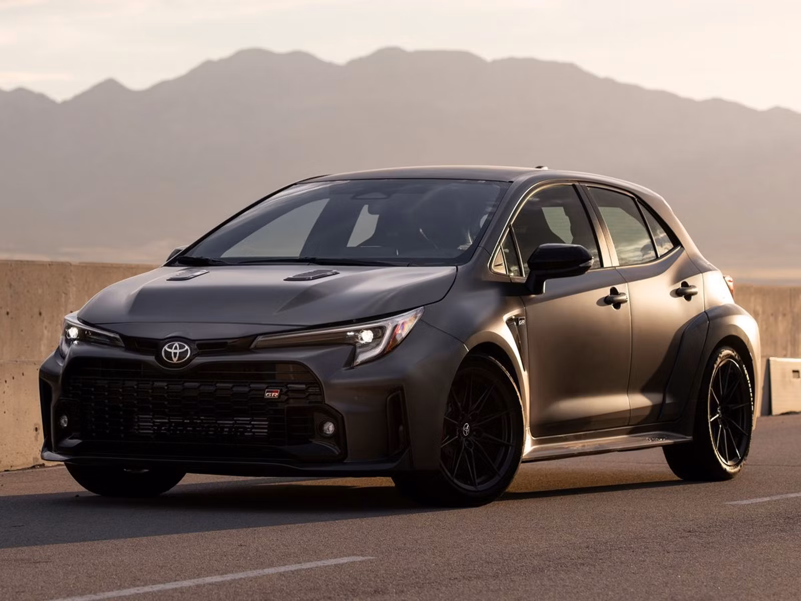 A sleek black sports car parked on a road with mountains in the background.