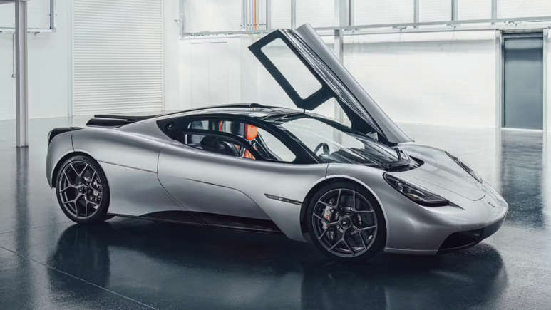 A sleek silver sports car with its gull-wing door open in a modern showroom.