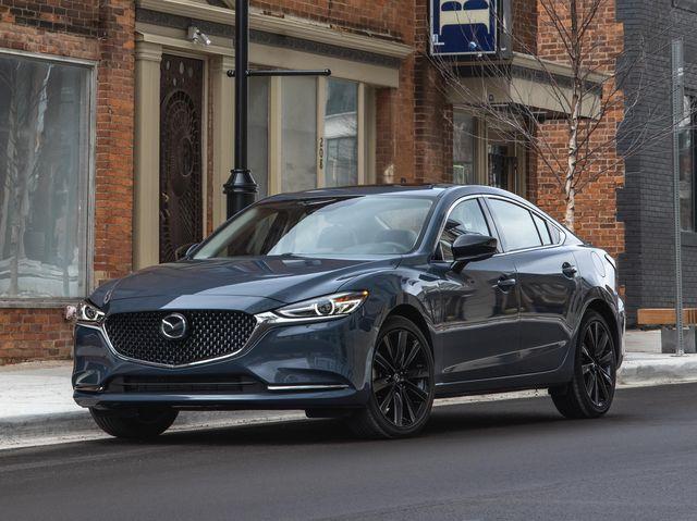 A dark blue Mazda sedan parked on a city street near brick buildings.