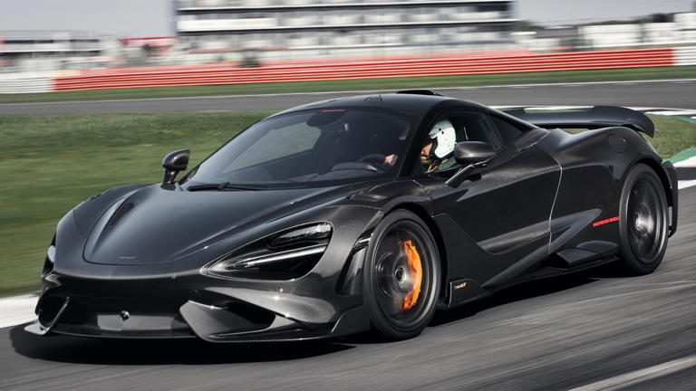 A black sports car speeding on a race track with a driver inside.