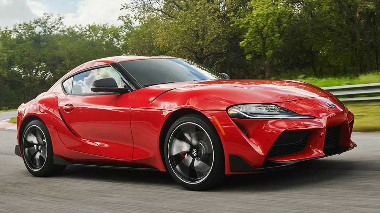A sleek red sports car parked outdoors with greenery in the background.