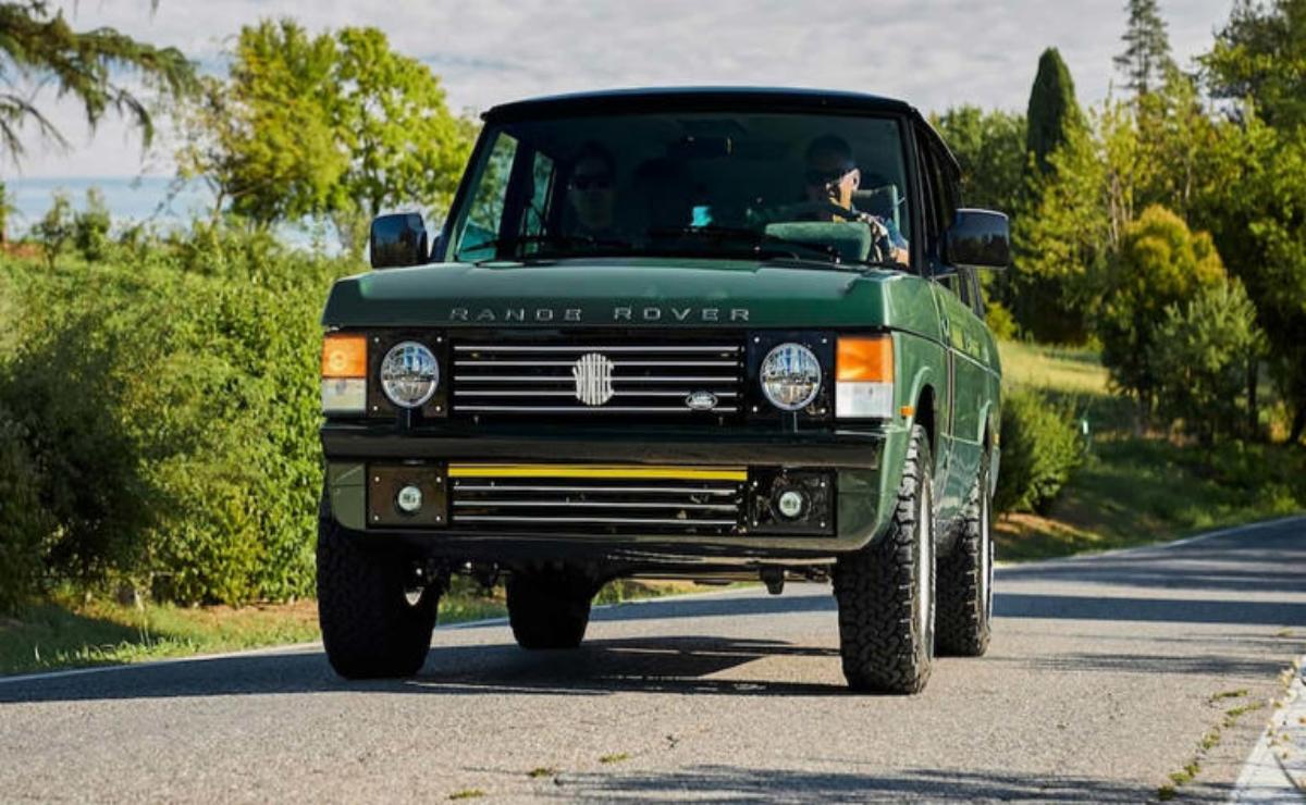 A green vintage SUV parked on a sunny road with trees in the background.
