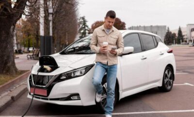 Man leaning on a white car, looking at his phone.