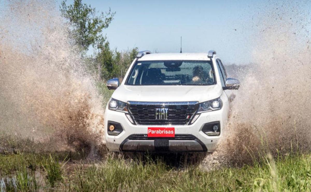 White pickup truck splashing through muddy terrain in a vigorous off-road drive.