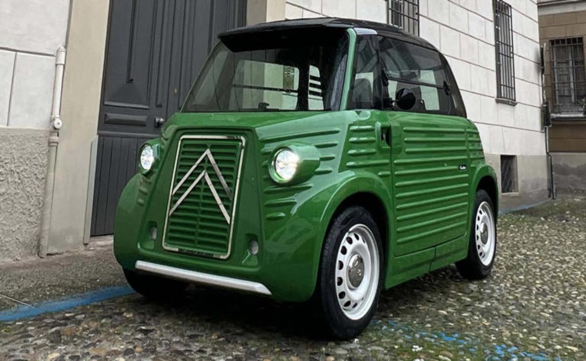 A vintage green Citroën 2CV car parked near a building.