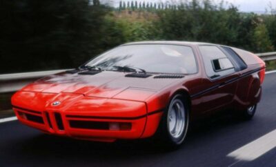 A sleek red sports car driving on a road with greenery in the background.