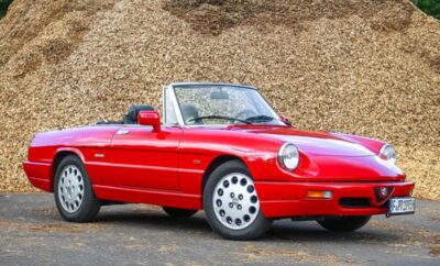 Classic red convertible sports car parked on gravel.