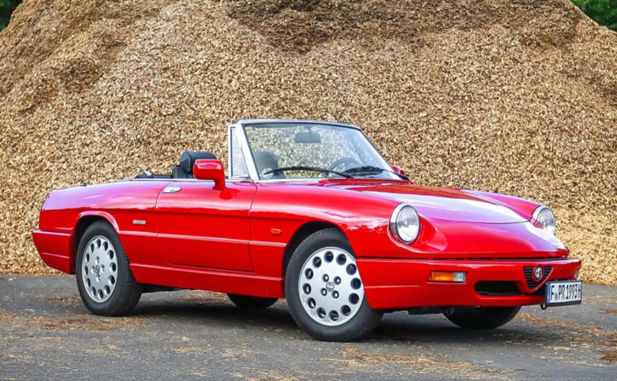 Classic red convertible sports car parked on gravel.