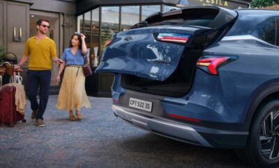 A woman walking near a parked blue SUV with an open trunk.