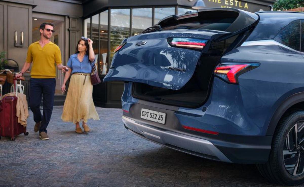A woman walking near a parked blue SUV with an open trunk.