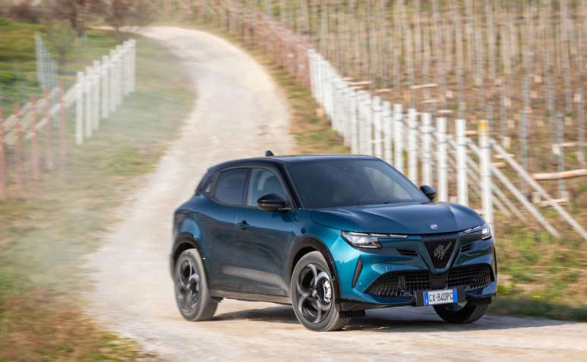 A sleek blue SUV parked on a country road beside a white fence.