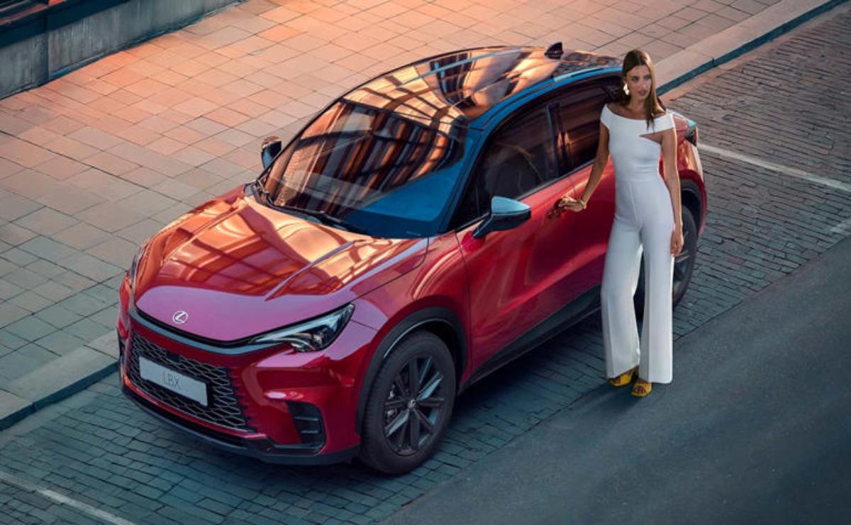 A woman in white stands next to a red electric SUV at sunset.