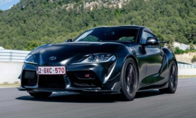 A sleek black BMW sports car driving on a road with greenery in the background.