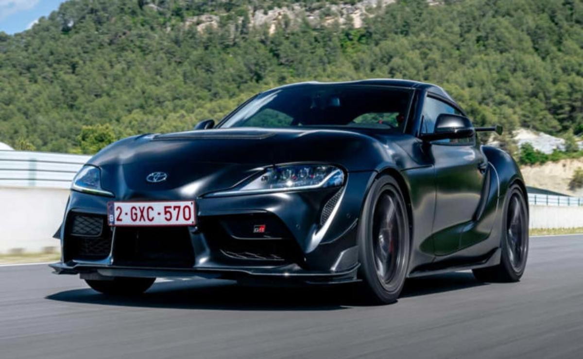 A sleek black BMW sports car driving on a road with greenery in the background.