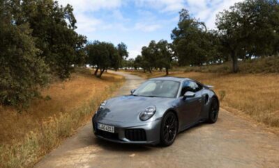 A sleek silver sports car on a rural dirt road surrounded by trees.