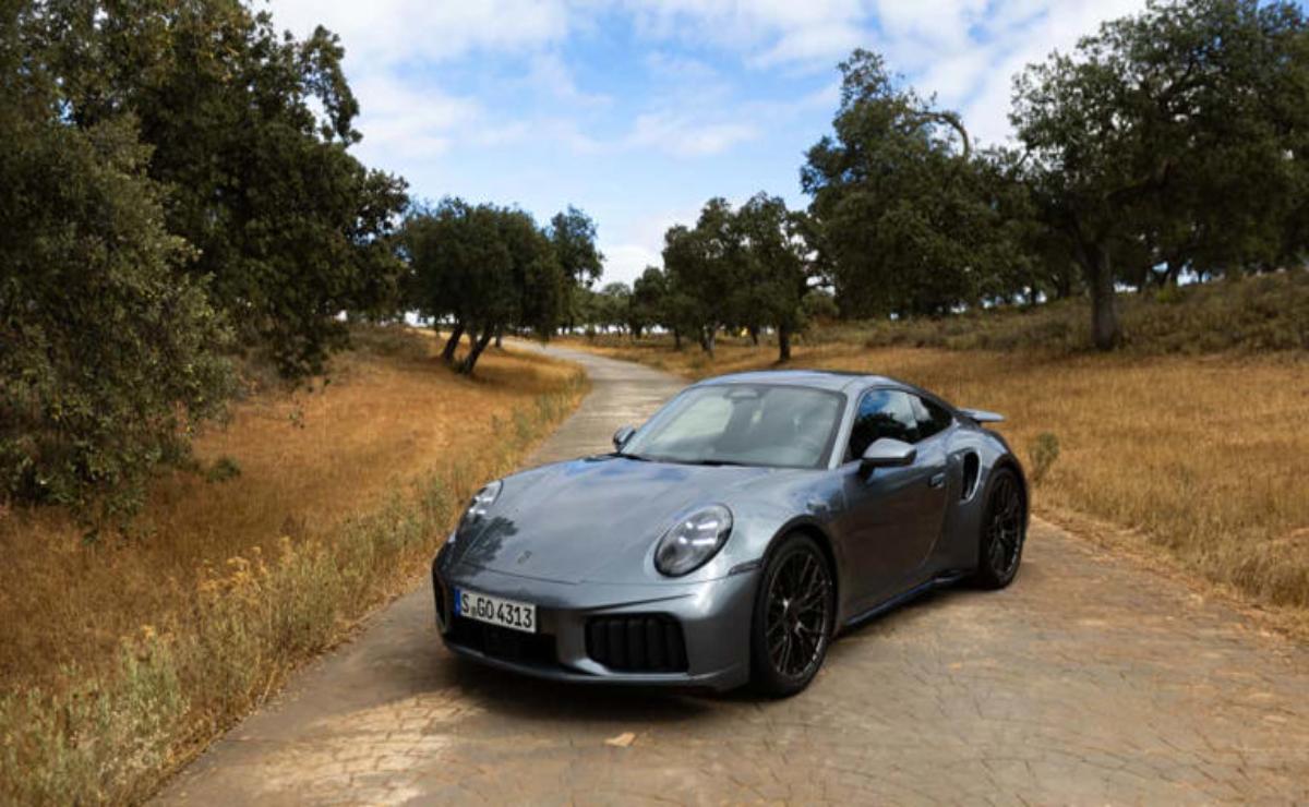 A sleek silver sports car on a rural dirt road surrounded by trees.