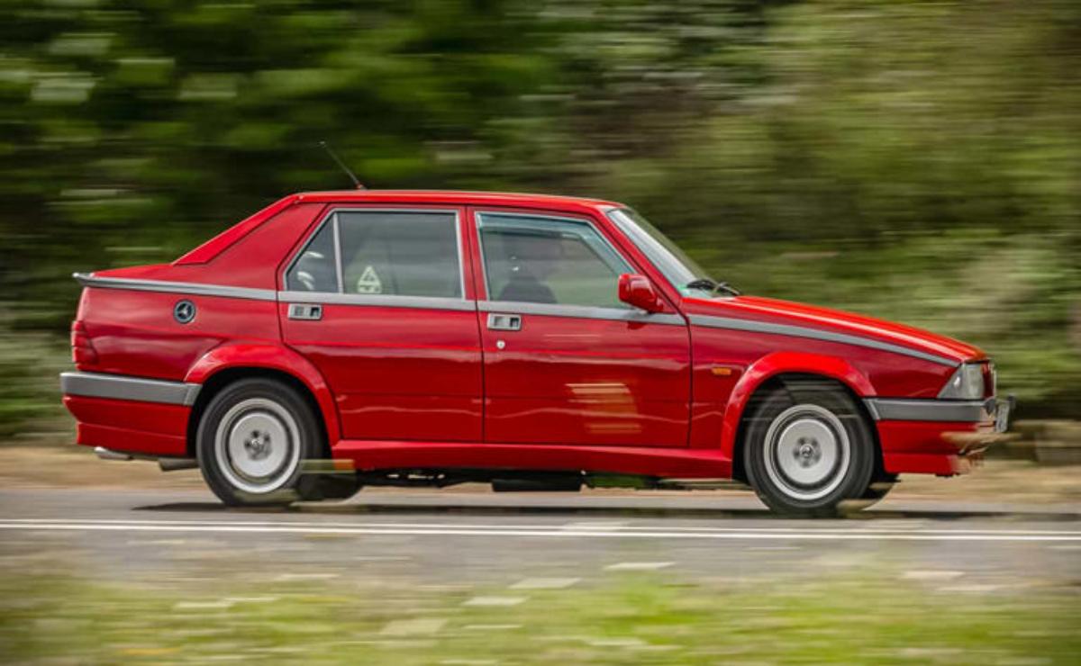 A red vintage car driving on a road with motion blur.