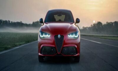 Red Alfa Romeo sports car on a foggy road with glowing headlights.