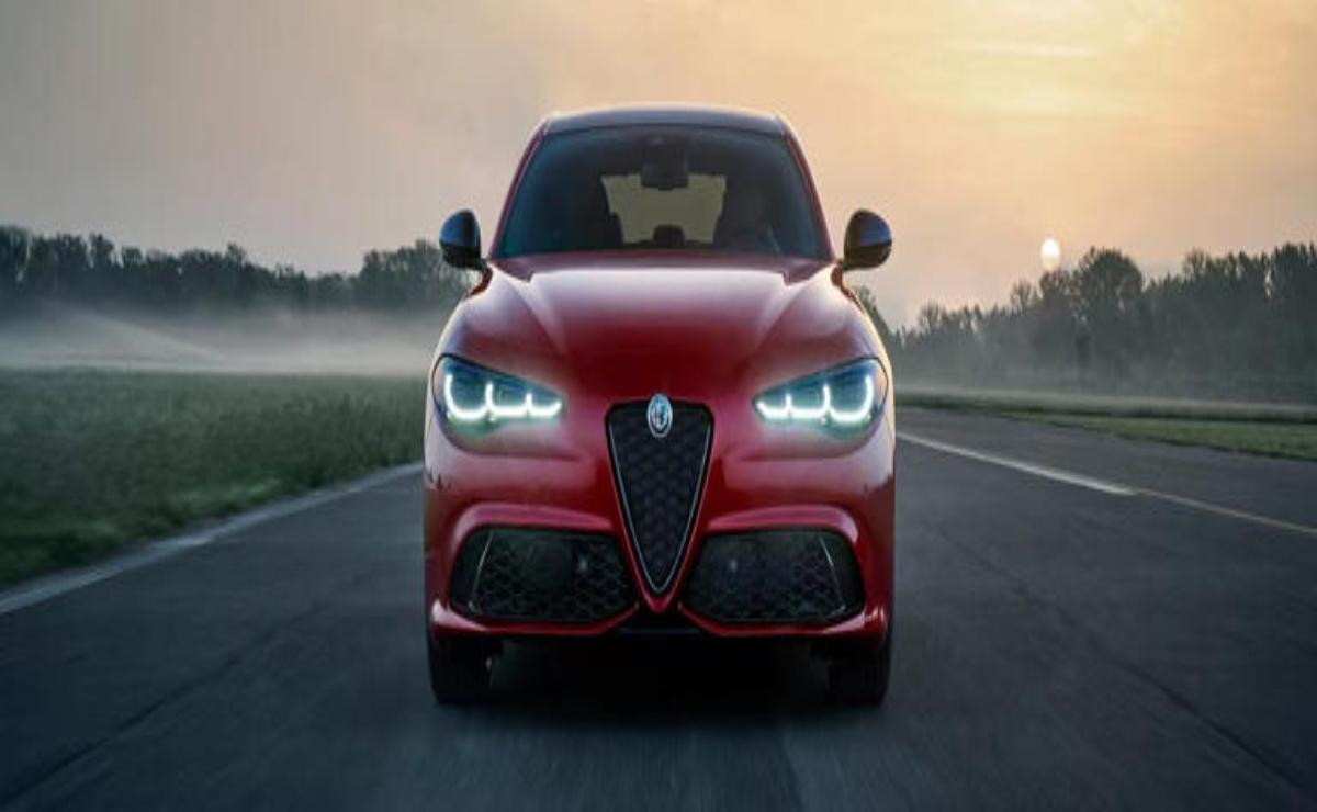 Red Alfa Romeo sports car on a foggy road with glowing headlights.