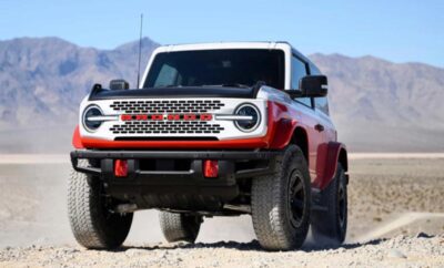 A rugged red and white off-road SUV parked on sandy terrain with mountains in the background.