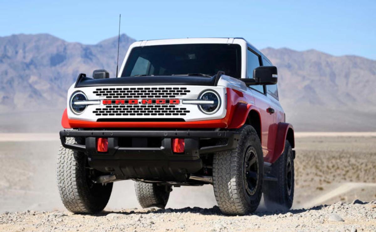 A rugged red and white off-road SUV parked on sandy terrain with mountains in the background.