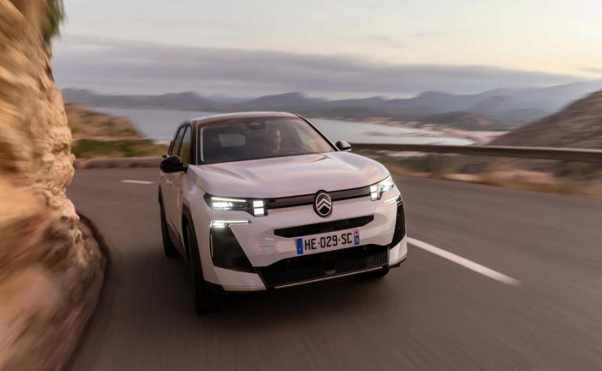 A white electric car driving on a scenic coastal road at sunset.
