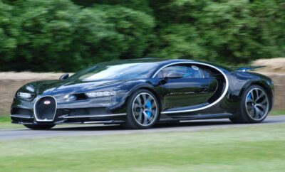 A sleek black Bugatti Chiron speeding on a road amidst greenery.