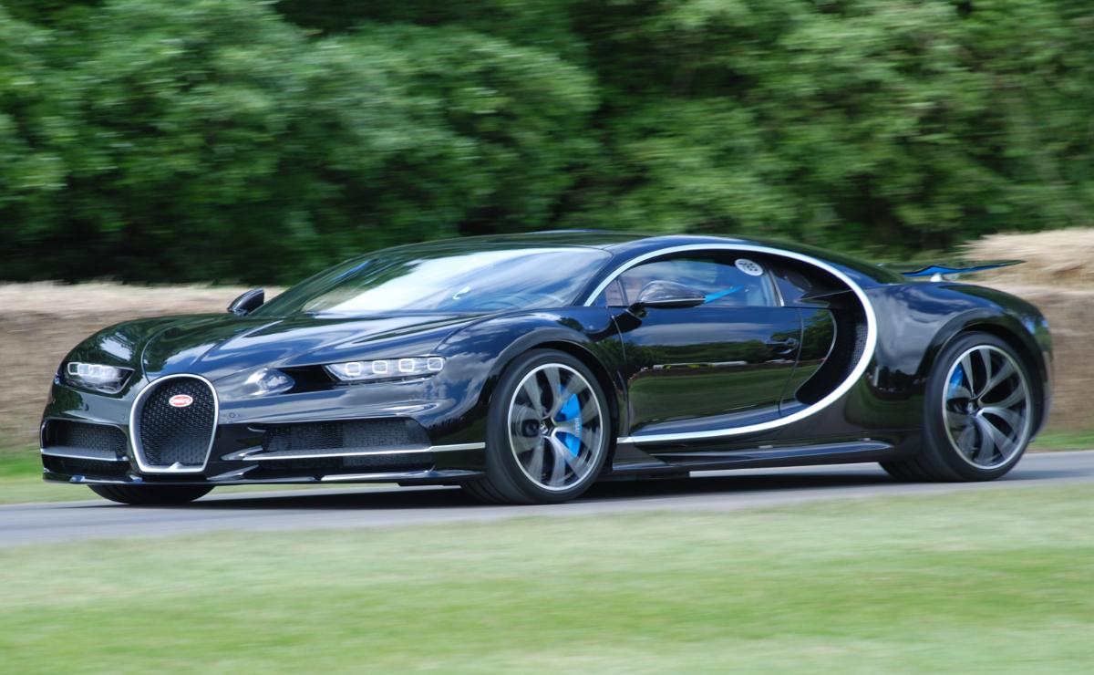 A sleek black Bugatti Chiron speeding on a road amidst greenery.