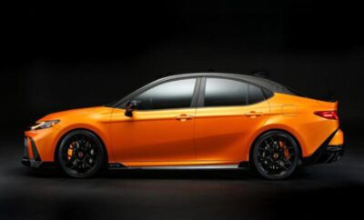 Sleek orange sports sedan with black wheels against a dark background.