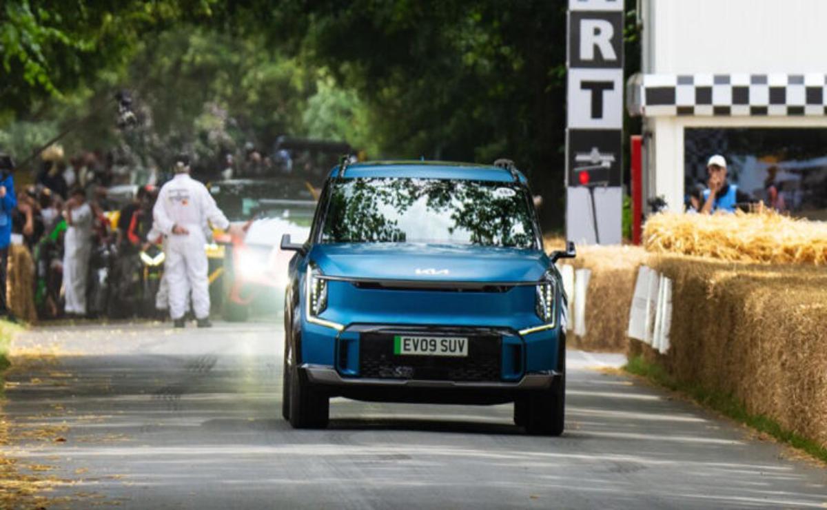 A blue electric SUV driving on a tree-lined road during a motorsport event.
